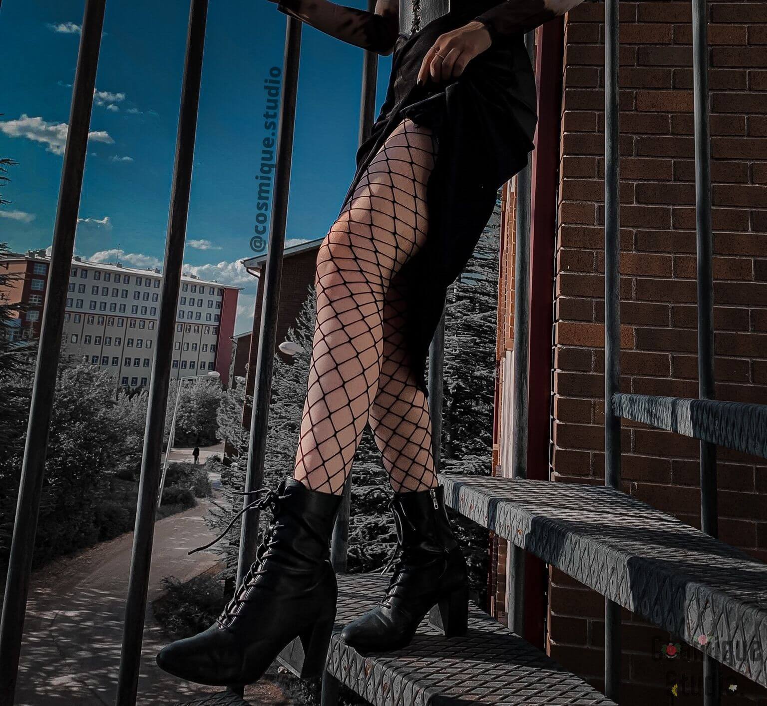 grunge aesthetic on the fire escape thick fishnet stockings under a black midi skirt combined with black leather heels 