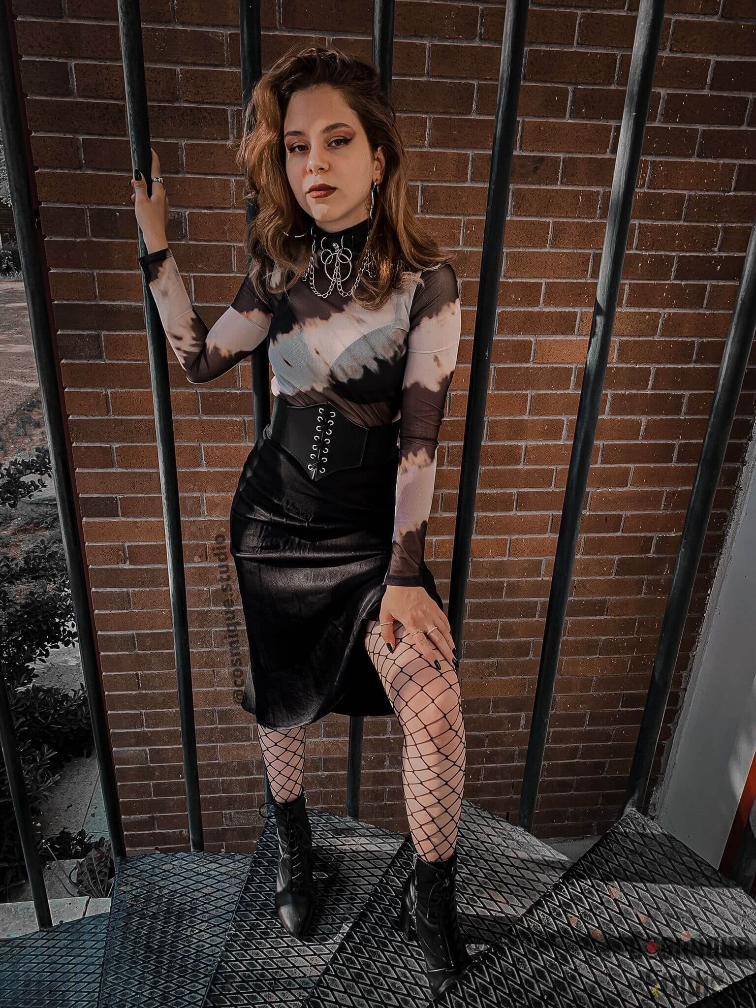 grunge girl standing on fire escape wearing animal print tulle blouse and black satin mini skirt completed with fishnet stockings, black leather corset and black leather choker 