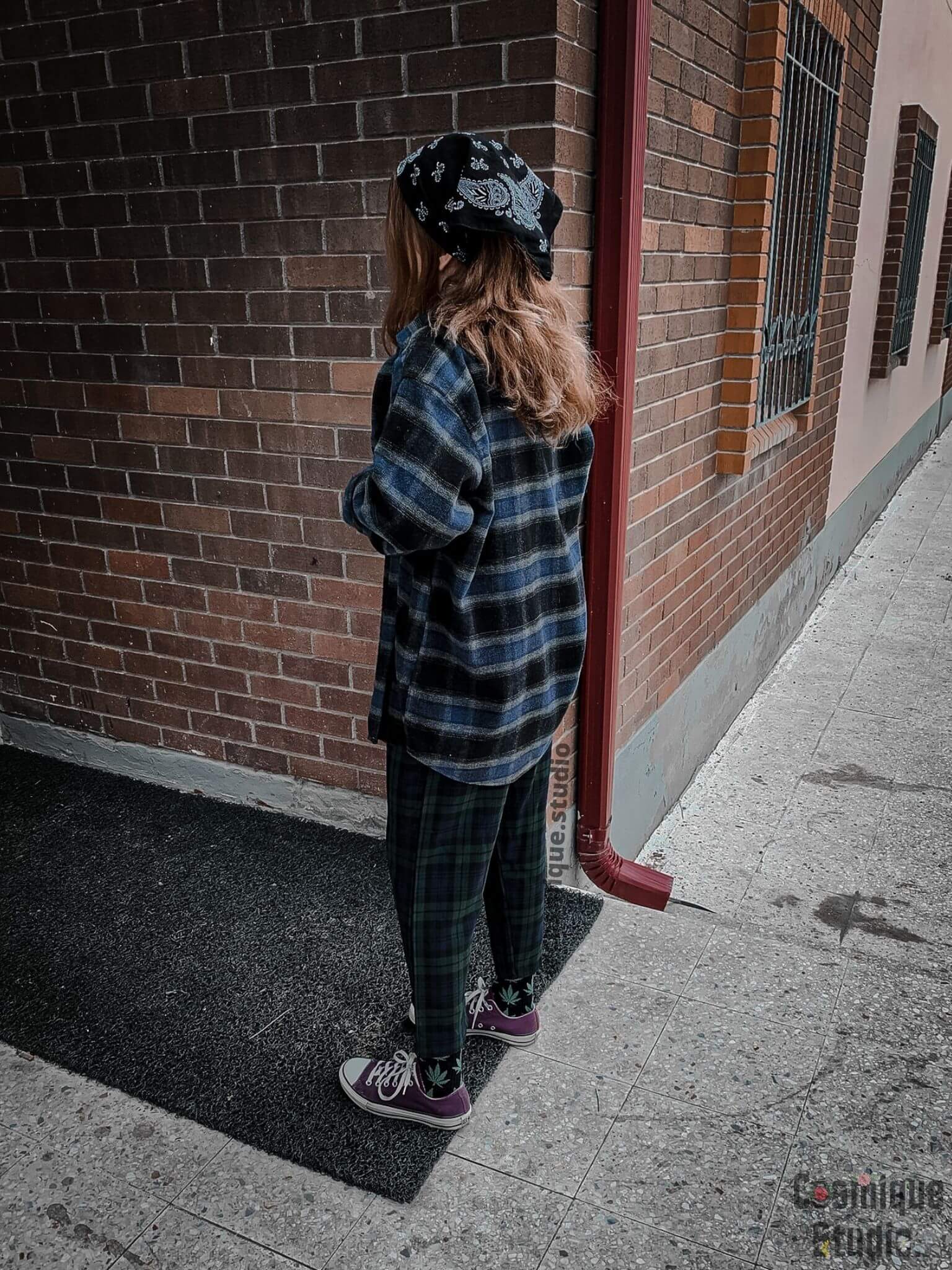 grunge girl on a tile wall wearing vintage blue lumberjack shirt, green baggy plaid pants, converse, completed with weed socks and bandana